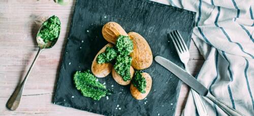 Salzkartoffeln mit einem Pesto aus Feldsalat auf einer schwarzen Schieferplatte vor hellgrauem Hintergrund, von oben fotografiert.