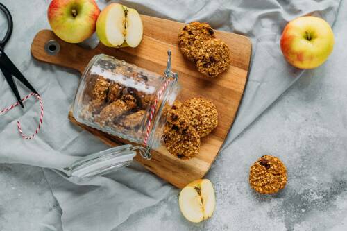 Früchteplätzchen mit Apfel und Karotte in Weckglas auf Schneidebrett neben Äpfeln vor hellem Hintergrund.