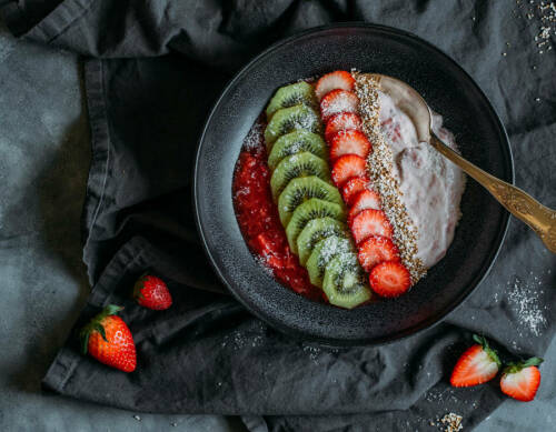 Frühstücksbowl mit Erdbeeren und Rhababer in Schüssel vor dunklem Hintergrund.
