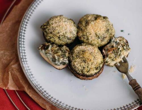 Gefüllte Riesen-Champignons auf weißem Teller mit Gabel vor dunklem Hintergrund.