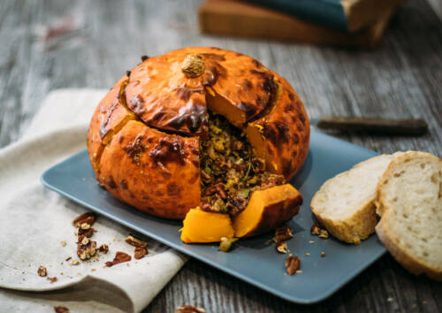 Herbstlich gefüllter Kürbis auf einer blauen Platte angeschnitten, daneben Weißbrot. Von oben fotografiert.