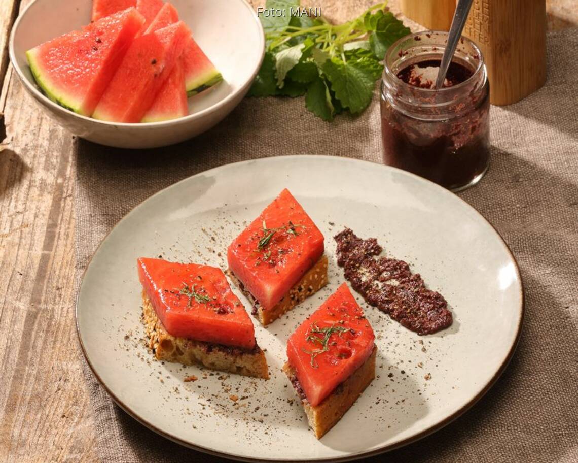 Teller mit gebratener Wassermelone, Olivnepaste auf Holztisch