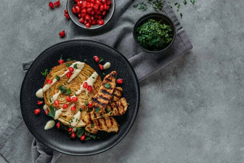 Geschmorter Weißkohl mit Putenstreifen auf einem schwarzen Teller mit Granatapfelkernen verziert.