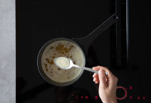 Geschmolzene Butter in Topf mit Löffel in Hand vor dunklem Hintergrund.