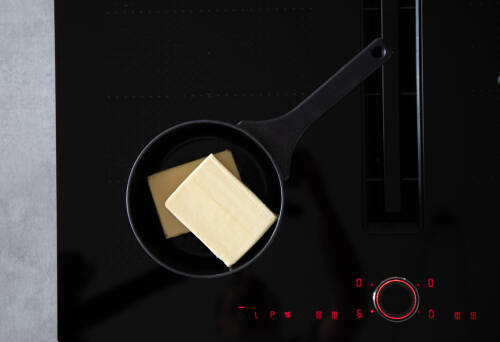 Butter im Topf auf Herd vor dunklem Hintergrund.