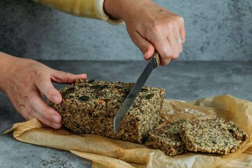 Selbst gebackenes Brot aus Hirseflocken, Kürbiskernen und Leinsamen wird angeschnitten.