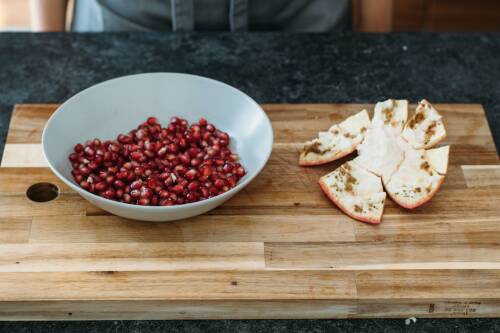 Fertig entkernter Granatapfel, leere Schale, volle Schüssel auf einem Holzbrett