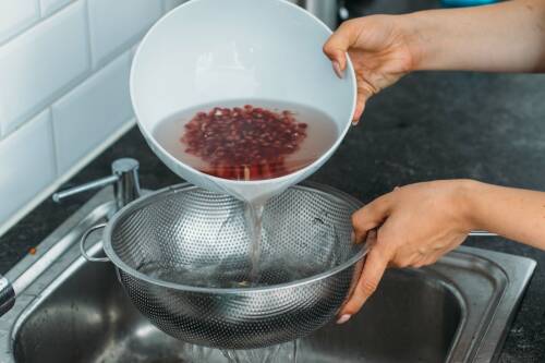 Abgießen der Granatapfelkerne in ein Sieb über dem Spülbecken
