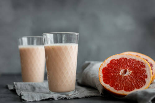 Grapefruit Smoothie in Gläsern neben Grapefruit vor dunklem Hintergrund.