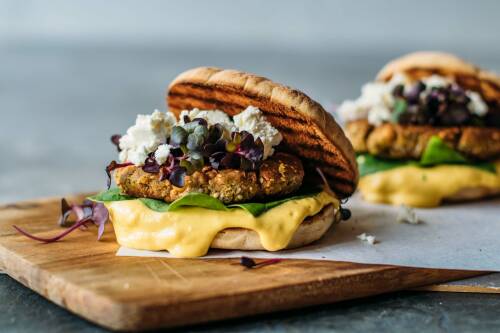 Leckeres vegetarisches Burger Patty im Bun mit leckerer Soße und Feta vor hellgrauem Hintergrund, von der Seite fotografiert.