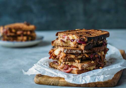Grilled Cheese Sandwich mit Birne und Cheddar auf Schneidebrett vor dunklem Hintergrund.