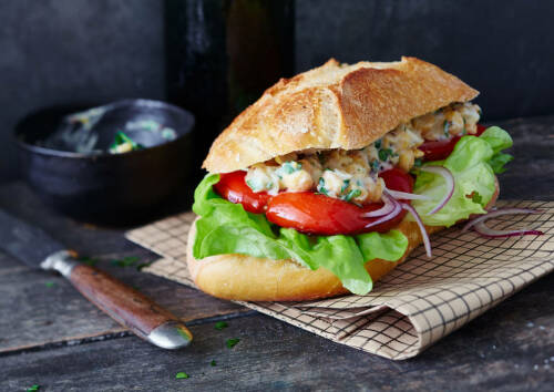 Sandwich mit gegrillter Paprika, Zwiebeln und Salat. Von vorne fotografiert.