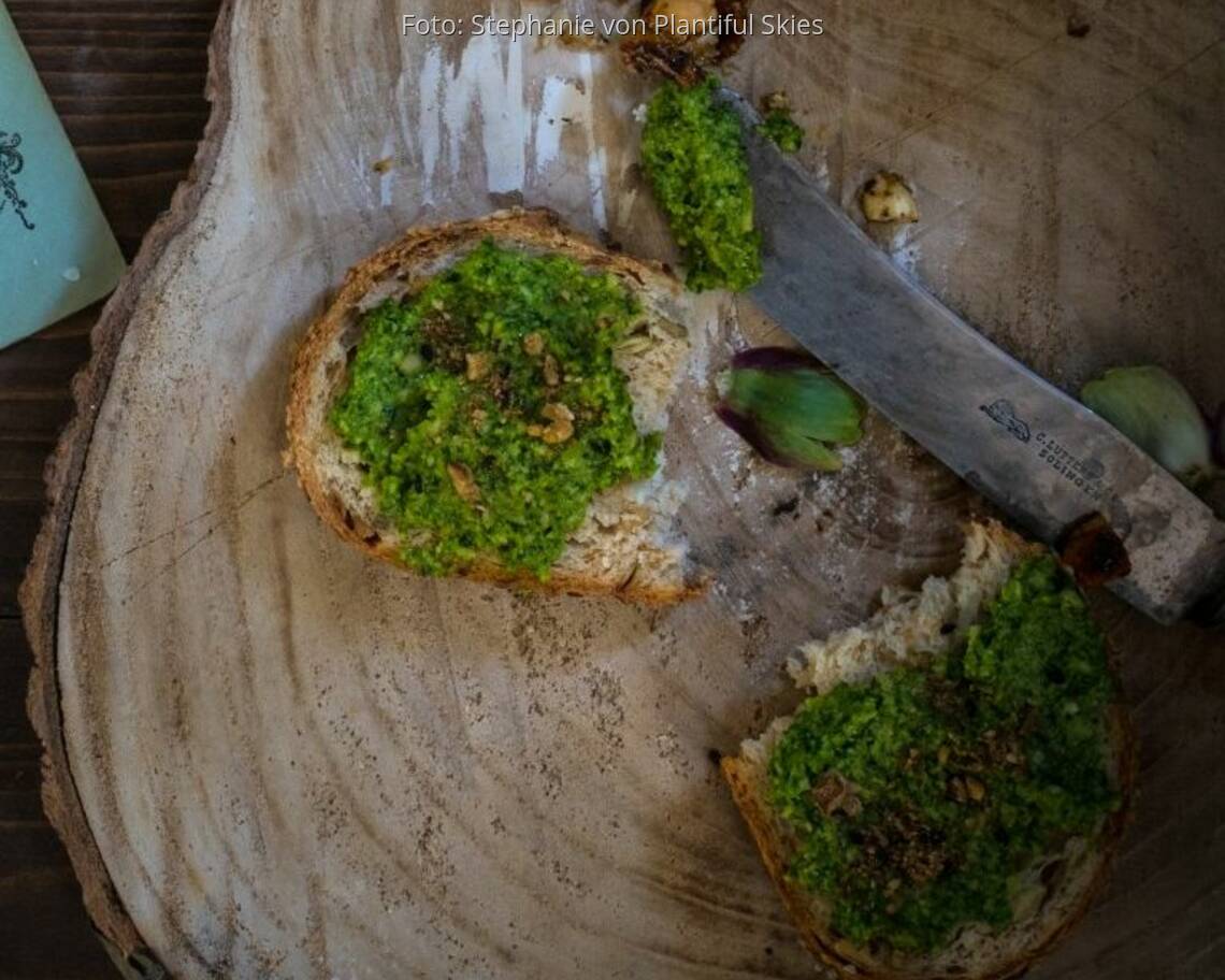 Holzscheibe mit zwei Brotscheiben mit Grünkohlpesto und Messer