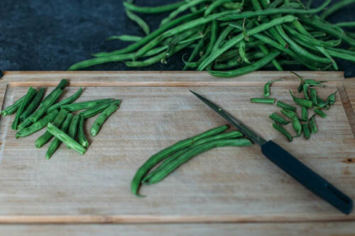 Grüne Bohnen auf einem Schneidebrett. Mit einem Messer werden die Spitzen abgeschnitten.