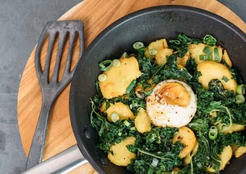 Gröstl mit Kartoffeln, Lauchzwiebeln, Grünkohl und Ei in einer Pfanne. Von oben fotografiert.