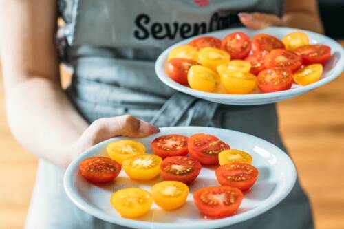 Schritt 4: Fertig halbierte Kirschtomaten auf einem weißen Teller, von vorne fotografiert.