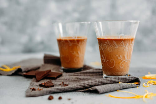Heiße Schokolade mit Orangenlikör in Gläsern neben Zartbitterschokolade vor hellem Hintergrund.