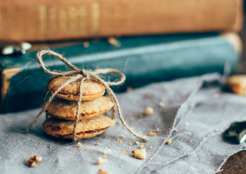 Herzoginplätzchen mit Nougat mit einer Schleife zusammengebunden, daneben Brösel. Von vorne fotografiert.