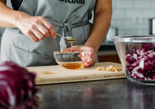 Honig wird mit einem Löffel in eine Schüssel gegeben. Die Schüssel steht auf einem Holzbrett. Daneben Radicchio.