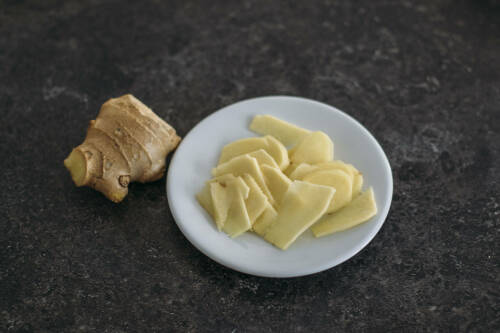 Ingwer aufgeschnitten auf Teller vor dunklem Hintergrund.