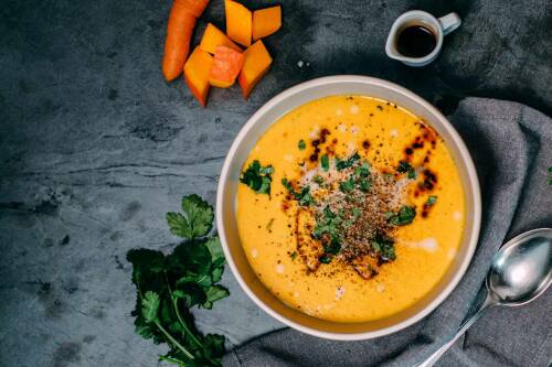 Ingwer-Kokos-Kürbissuppe mit Petersilie und Karotten vor dunklem Hintergrund.
