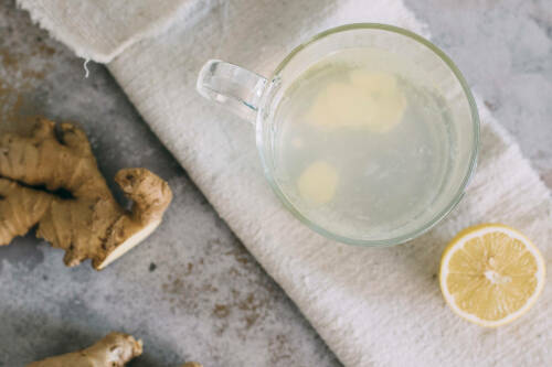 Ingwer Zitronen Tee in Glas neben Ingwer und Zitrone vor hellem Hintergrund.