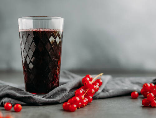 Johannisbeersaft in Glas neben Johannisbeeren vor grauem Hintergrund.