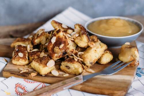 Kaiserschmarrn mit karamellisierten Mandeln auf einem Holzbrett, dahinter eine Schüssel mit Apfelmus.
