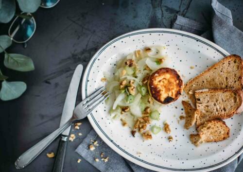 Karamellisierter Fenchel mit gebräuntem Ziegenkäse und knusprigem Brot auf einem Teller. Von oben fotografiert.