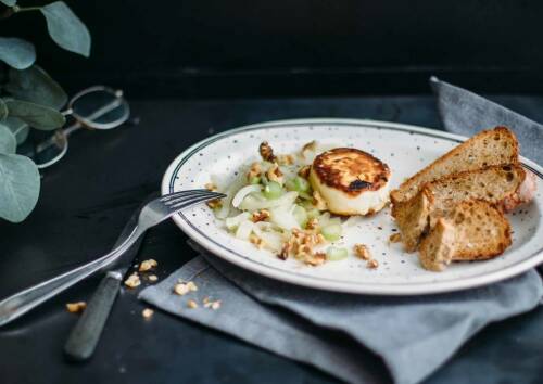 Karamellisierter Fenchel mit Ziegenkäse und geröstetem Brot auf einem weißen Teller vor dunklem Hintergrund