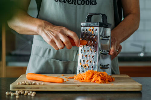 Karotten in Händen mit Reibe vor hellem Hintergrund,
