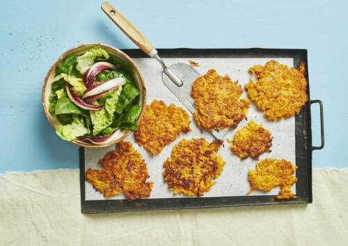 Leckere Puffer mit Salat dazu auf einem Blech vor blauem Hintergrund, von oben fotografiert.