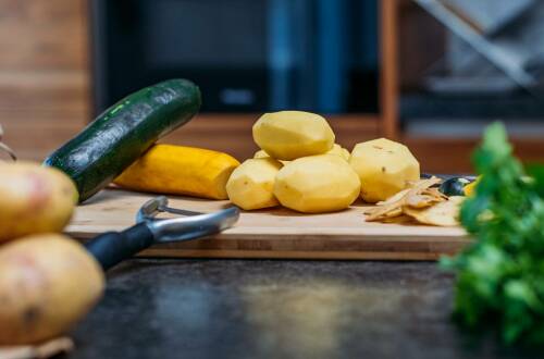 Kartoffeln mit Zucchini auf Schneidebrett vor hellem Hintergrund.
