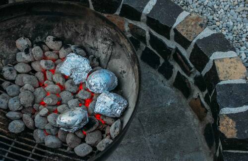 Kartoffeln aus der Glut im Grill neben Kies vor dunklem Hintergrund.