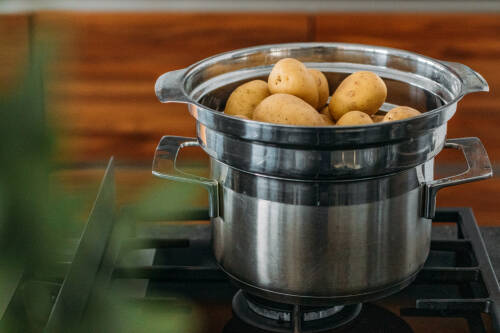 Kartoffeln Dämpfen in Dampfgarer auf Gasherd vor dunklem Hintergrund.