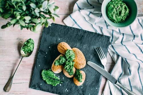 Pellkartoffeln mit Salz und Feldsalatpesto auf einer Schieferplatte, daneben Besteck. Von oben fotografiert.
