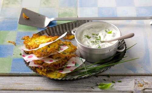 Kartoffelpuffer mit Kräutercreme neben Schnittlauch vor hellem Hintergrund.