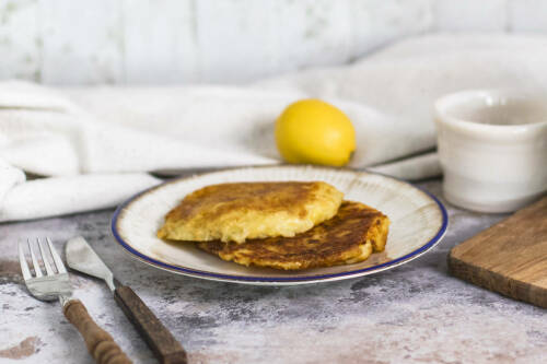 Kartoffelpuffer mit Sauerkraut auf weißem Teller neben Besteck und Becher vor hellem Hintergrund.