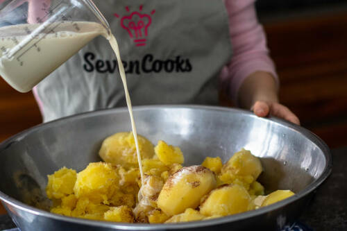 Kartoffeln in Schüssel mit Mandelmilch und Muskatnuss vor dunklem Hintergrund.