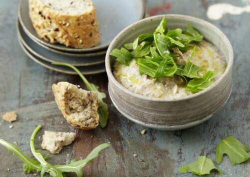 Hummus aus Esskastanien in einer kleinen Schüssel mit Rucola garniert, dazu gibt es Brot. Von oben fotografiert.