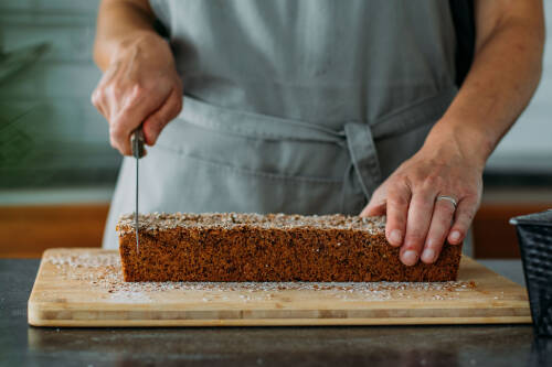 Kichererbsenbrot auf Schneidebrett mit Händen vor dunklem Hintergrund.