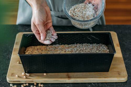 Kichererbsenbrot in Kastenform mit Händen vor dunklem Hintergrund.