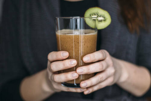 Kiwi Papaya Sport Shake für Figurbewusste in Händen vor dunklem Hintergrund.