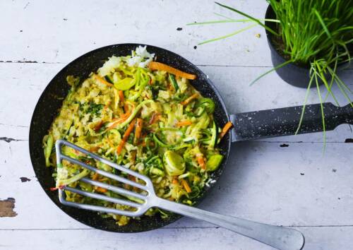 Bratreis mit Lauch in einer schwarzen Pfanne auf weißem Holz, von oben fotografiert