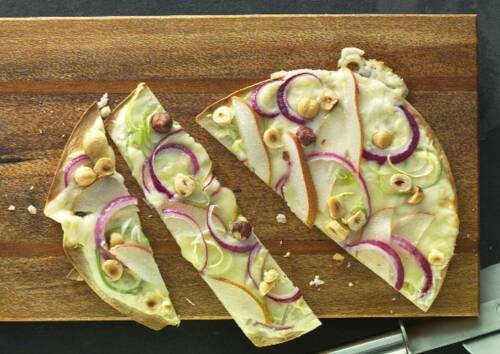 Flammkuchen mit Lauch und Zwiebel in drei Stücke unterteilt auf einem braunen Schneidebrett