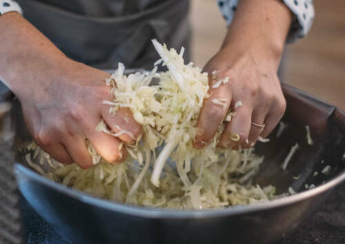 Kohlstreifen werden in einer Metallschüssel mit den Händen geknetet.