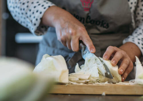 Ein Kohl wird auf einem Holzbrett in feine Streifen geschnitten.