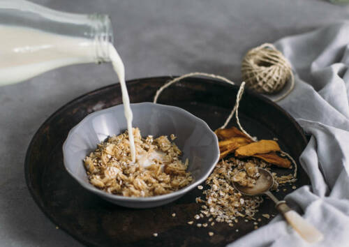 Selbstgemachtes Kokos-Mandel-Müsli in einer Schüssel, während es mit Milch übergossen wird.