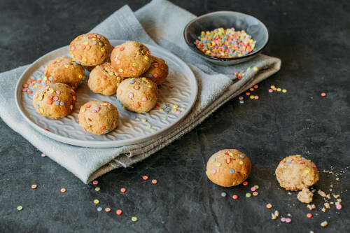 Konfettikekse mit Konfetti auf Geschirrtuch vor dunklem Hintergrund.