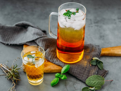 Kräuter Limonade in Glas und Karaffe neben Kräutern vor dunklem Hintergrund.